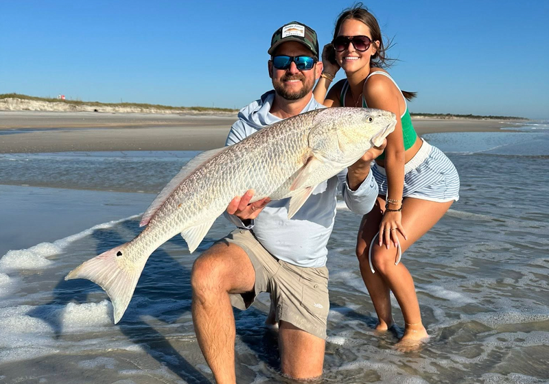 Man and woman holding a large fish on a beach